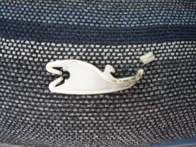 Broken white plastic clip on dark textured fabric. Small piece of clip is detached