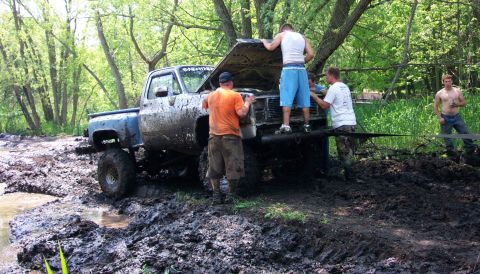 1978 Ford Bronco - Several men attempt to free a heavily mud-caked pickup truck from a mire in a wooded area.