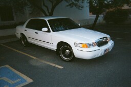 2001 Mercury Grand Marquis - A white 2001 Mercury Grand Marquis is parked in a handicapped spot next to a building.