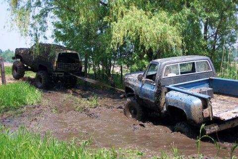 1978 Ford Bronco - Two trucks struggle in the mud, one being towed out of a ditch by another.