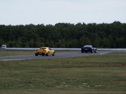 2001 Mercury Grand Marquis - Two cars are on a race track, with a line of trees behind them and a cloudy sky above.