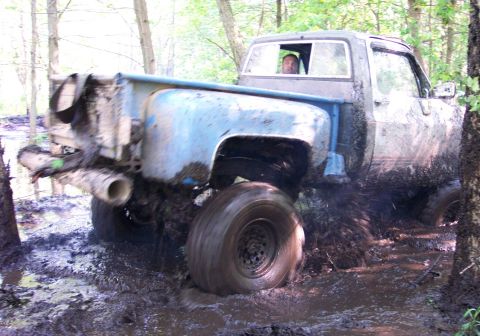 1978 Ford Bronco - A pickup truck navigates a challenging muddy terrain in a wooded area.