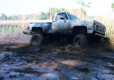 1978 Ford Bronco - Pickup truck navigating a muddy terrain, kicking up dirt and water.