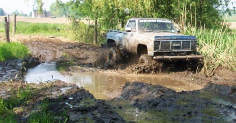 1978 Ford Bronco - Modified GMC pickup truck powers through a challenging mud bog on a rural track.