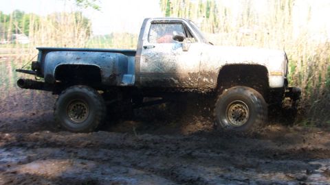 1978 Ford Bronco - This pickup truck is navigating a muddy terrain, kicking up dirt and water.