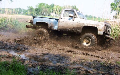 1978 Ford Bronco - A white pickup truck navigates a muddy terrain, kicking up dirt and water.