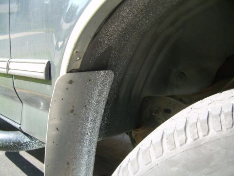 1992 Ford Bronco - The wheel well of a vehicle is covered in sand, with a mud flap and tire visible.