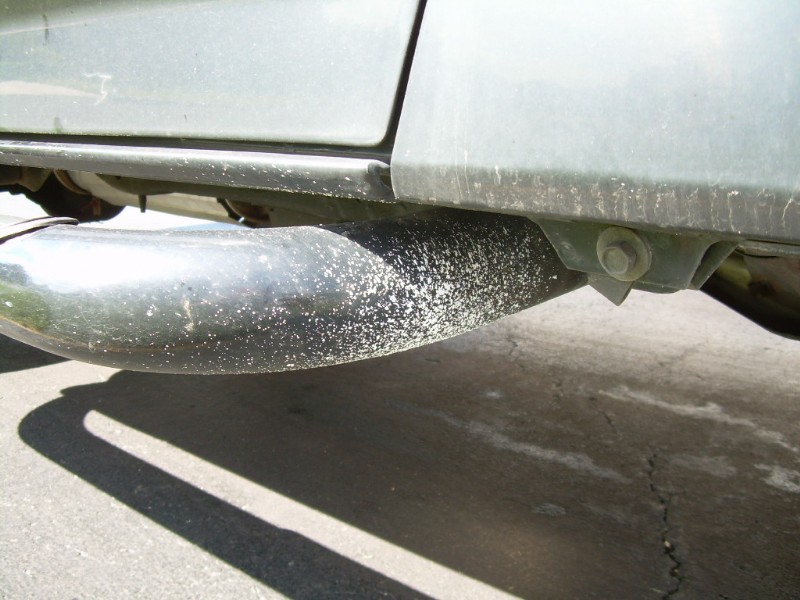Exhaust pipe with white residue under a gray vehicle's undercarriage