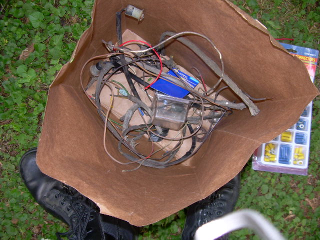Paper bag full of old wiring harness pieces on grass, with a wire connector kit nearby