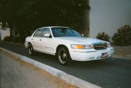 2001 Mercury Grand Marquis - A white 2001 Mercury Grand Marquis is seen from a three-quarter front view, parked on a paved surface next to a curb.