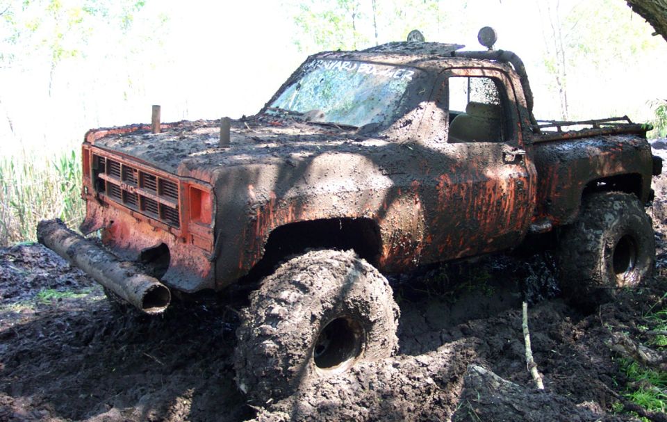 Mud-covered 1979 pickup truck stuck in deep mud, with large tires and a custom pipe bumper