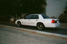 2001 Mercury Grand Marquis - White 2001 Mercury Grand Marquis parked on a street next to a curb and sidewalk.