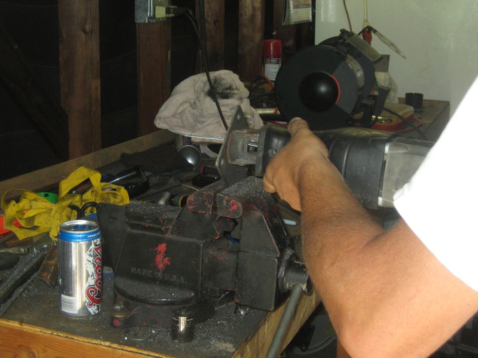 Workbench with a vise holding a metal part, a grinder, and a can of Coors Light