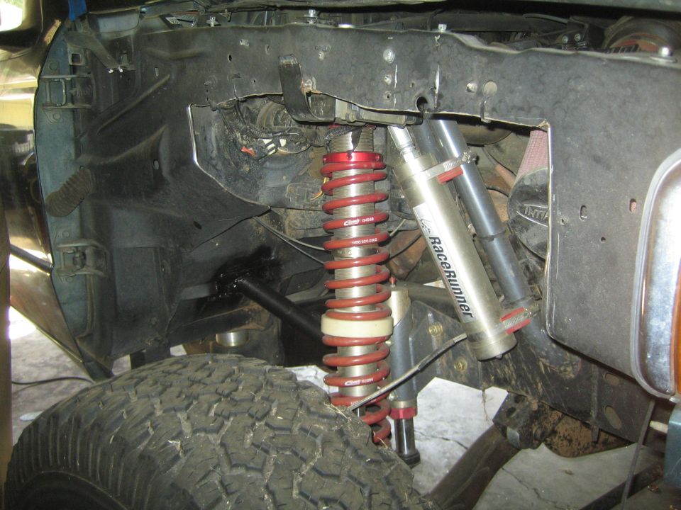 Off-road suspension with red coilover shocks and silver RaceRunner shocks mounted to a dirty frame. A large tire is visible