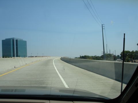 1995 Ford Taurus - View from a vehicle driving on a highway under a clear blue sky, passing a large glass office building.