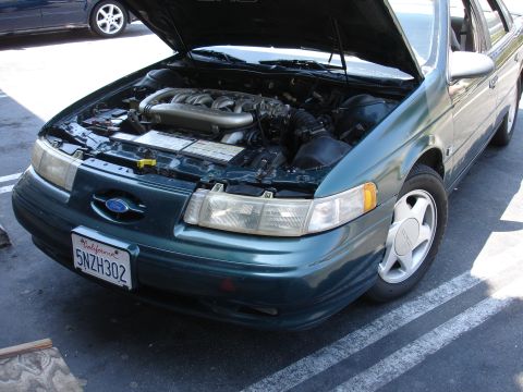 1995 Ford Taurus - The front of a green 1996 Ford Taurus is shown with the hood open, revealing the engine compartment.
