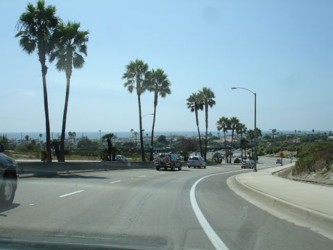 1995 Ford Taurus - Coastal highway scene with palm trees and vehicles on a clear day.