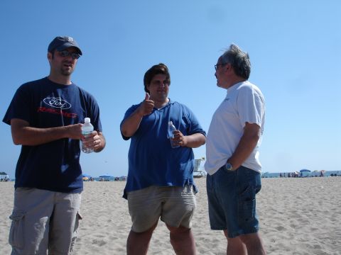 1995 Ford Taurus - Three men converse on a beach, with one man wearing a Ford branded t-shirt.