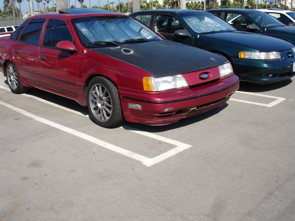 Red 1995 Ford Taurus with black hood and aftermarket wheels parked in a lot