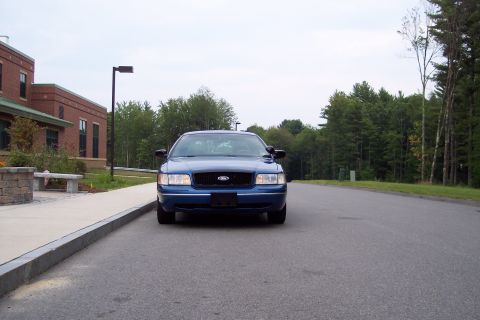 2001 Ford Crown Victoria - Front view of a blue 2001 Ford Crown Victoria parked on a road next to a building.