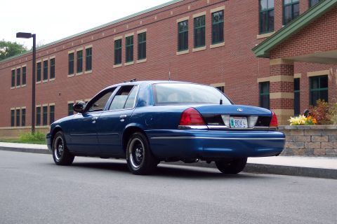 2001 Ford Crown Victoria - A blue 2001 Ford Crown Victoria is parked on the street in front of a brick building.