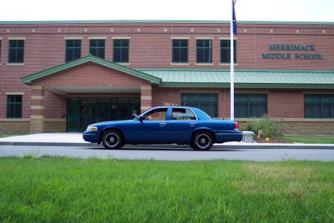 2001 Ford Crown Victoria - A blue 2001 Ford Crown Victoria is parked on the side of the road in front of a brick school building.