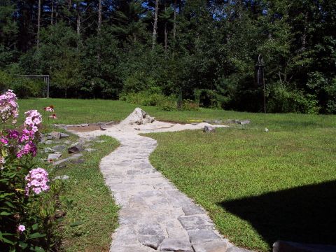 2001 Ford Crown Victoria - A backyard scene shows a winding stone path leading towards a sand pit area with some rocks and landscaping in-progress landscaping.