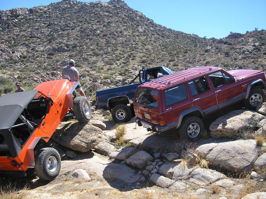 Orange Jeep, blue pickup, and red SUV off-roading over rocks