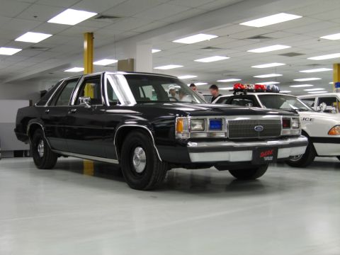 2001 Ford Crown Victoria - A black police car with a DARE logo on the front bumper is parked indoors next to other police vehicles.
