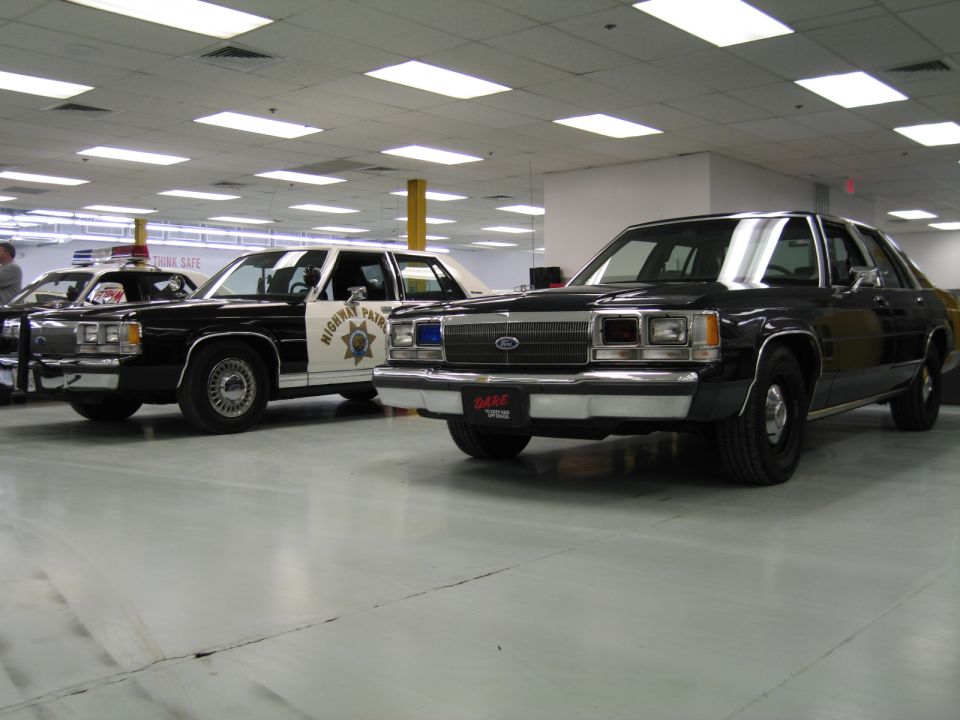 Black unmarked Ford LTD Crown Victoria with DARE plate beside a CHP black-and-white