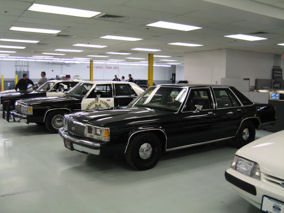 Black Ford LTD Crown Victoria police sedans displayed indoors with a Highway Patrol car