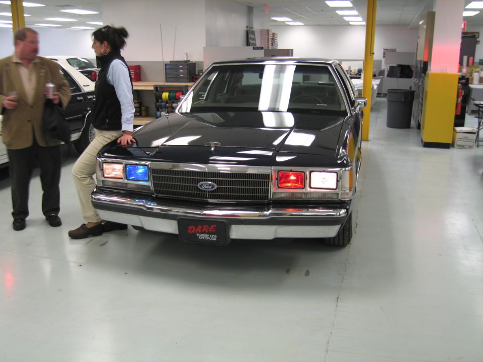 Front view of a dark 2001 Ford Crown Victoria with DARE license plate and red/blue lights