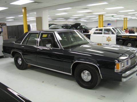 2001 Ford Crown Victoria - A black sedan is parked indoors, with a police car visible in the background.