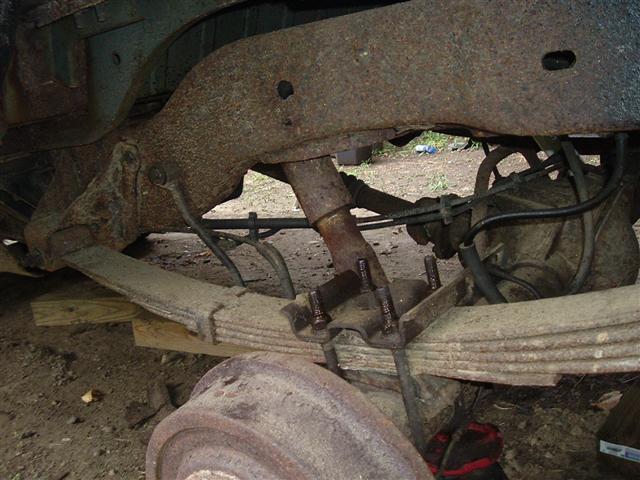 Rear axle and leaf spring suspension of a vehicle, showing rust and wear. Part of a Supermotors.net watermark is visible