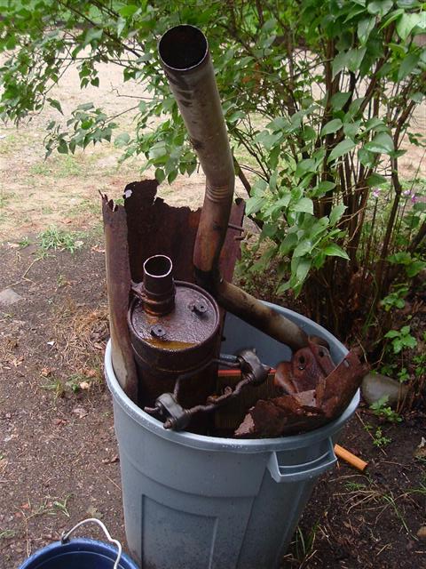 1991 Ford Bronco - Discarded exhaust system components are piled into a gray trash can outdoors.