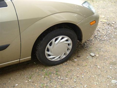 1991 Ford Bronco - Close-up of a gold car's front fender and wheel, parked on a gravel surface.
