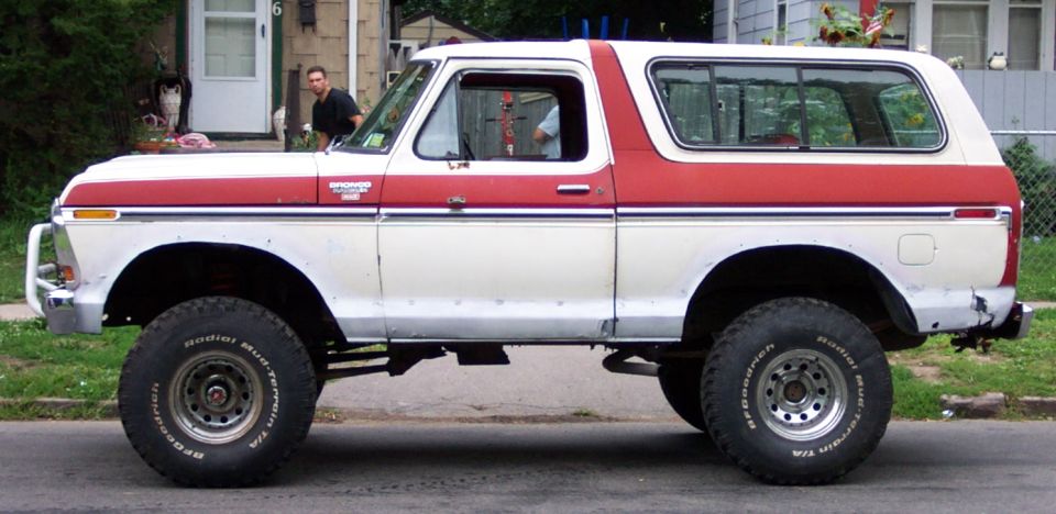 Lifted white and red Ford Bronco with off-road tires parked on a street