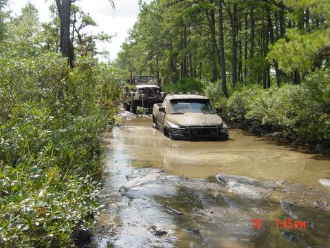 1995 Dodge 1500 - Two off-road vehicles navigate a challenging muddy trail through a wooded area.