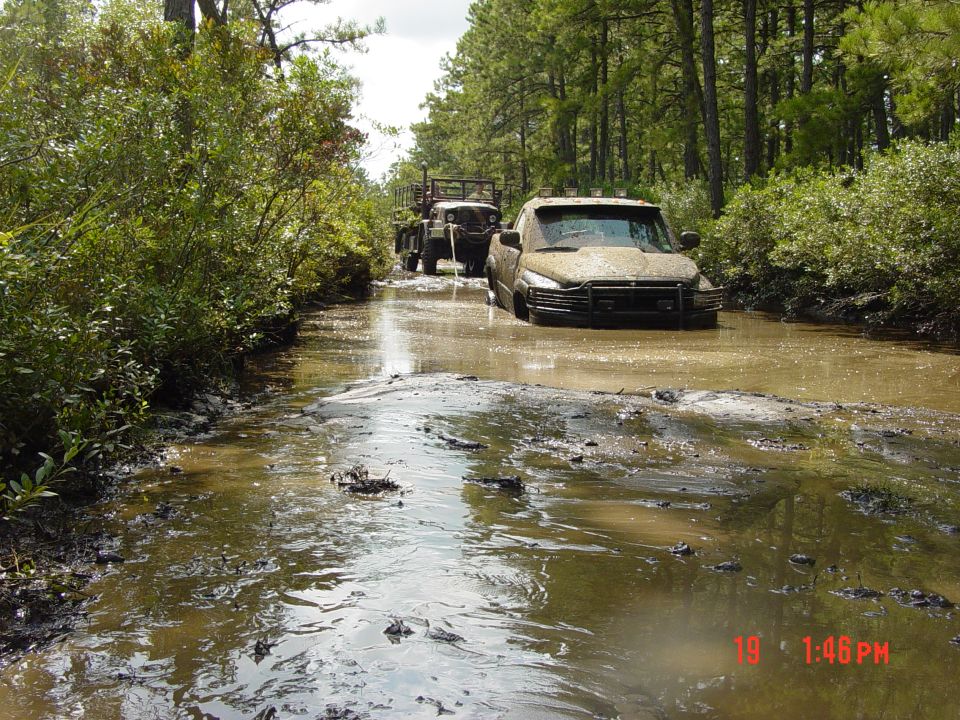Muddy 1995 Dodge 1500 stuck in water, front view. Another truck behind