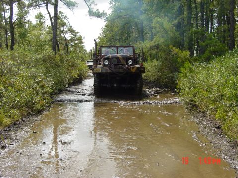 1995 Dodge 1500 - A military truck navigates a water-filled, muddy path surrounded by dense trees.