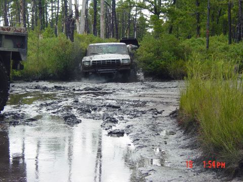 1995 Dodge 1500 - Two trucks navigate a challenging muddy terrain surrounded by dense forest vegetation.