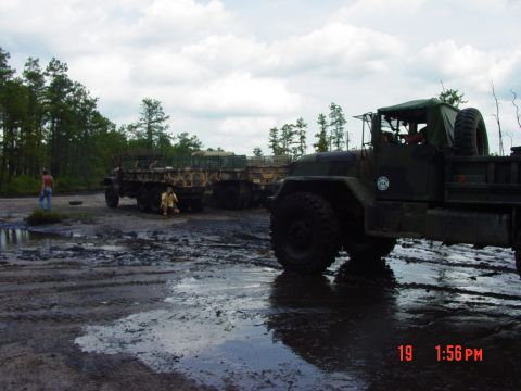 1995 Dodge 1500 - Several military trucks are parked in a muddy, wet area with trees in the background.