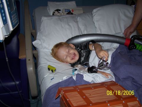 1979 Ford F-150 - A young child with red hair laughs joyfully while lying in a hospital bed, clutching a toy sword and surrounded by medical equipment.