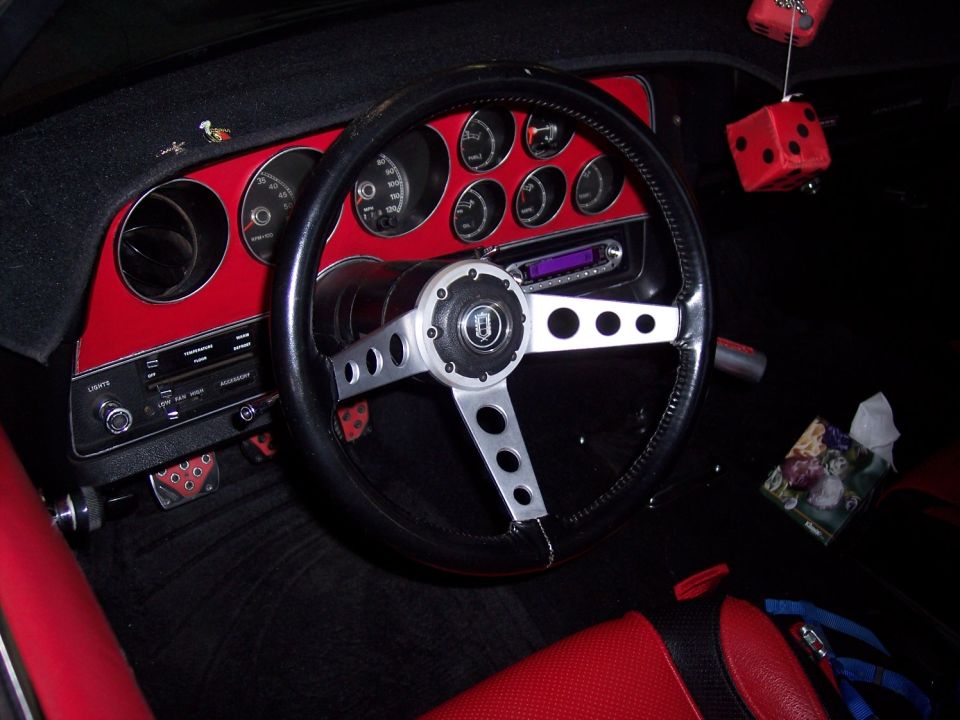 Car interior with red accents, aftermarket steering wheel, and fuzzy dice hanging from the rearview mirror
