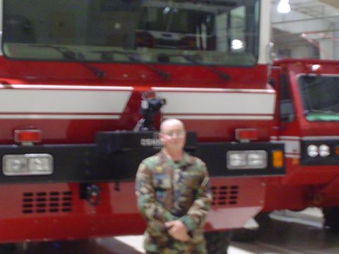 1981 Ford Bronco - A person in military uniform stands before a large red fire truck, with another vehicle visible to the right.