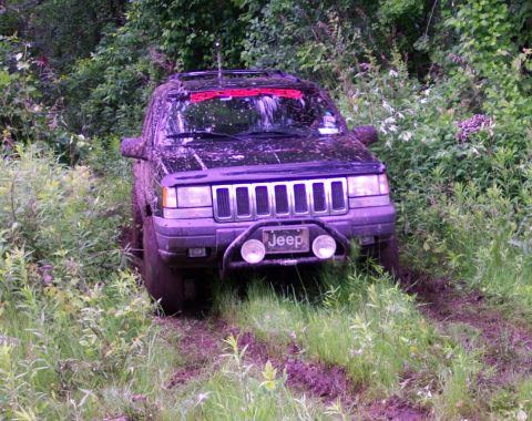 1978 Ford Bronco - A black Jeep Grand Cherokee is stuck in the mud off-road.