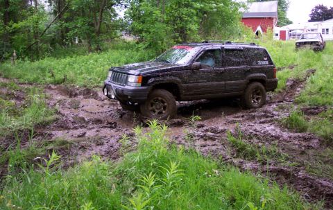 1978 Ford Bronco - Jeep Grand Cherokee navigating a muddy trail, with another vehicle in the distance.