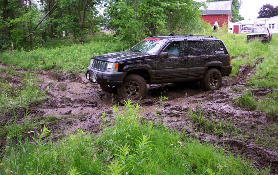 Black Jeep Grand Cherokee stuck in mud on a trail, another vehicle visible in background