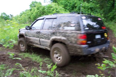 1978 Ford Bronco - A black Jeep Grand Cherokee navigates a muddy off-road trail.