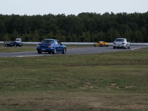 2001 Mercury Grand Marquis - Multiple vehicles are captured on a paved track with a wooded area in the distance and a watermark at the bottom right.